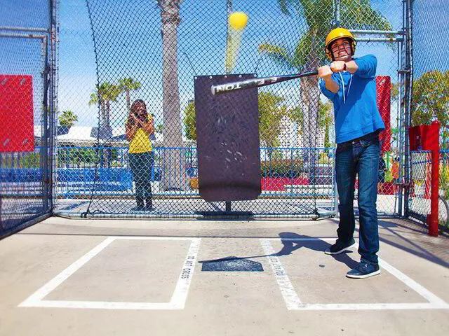 A man in a batting cage swinging a bat, with a woman in the background