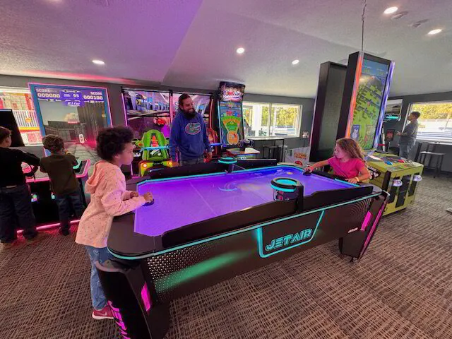 A children play air hockey in a brightly lit arcade